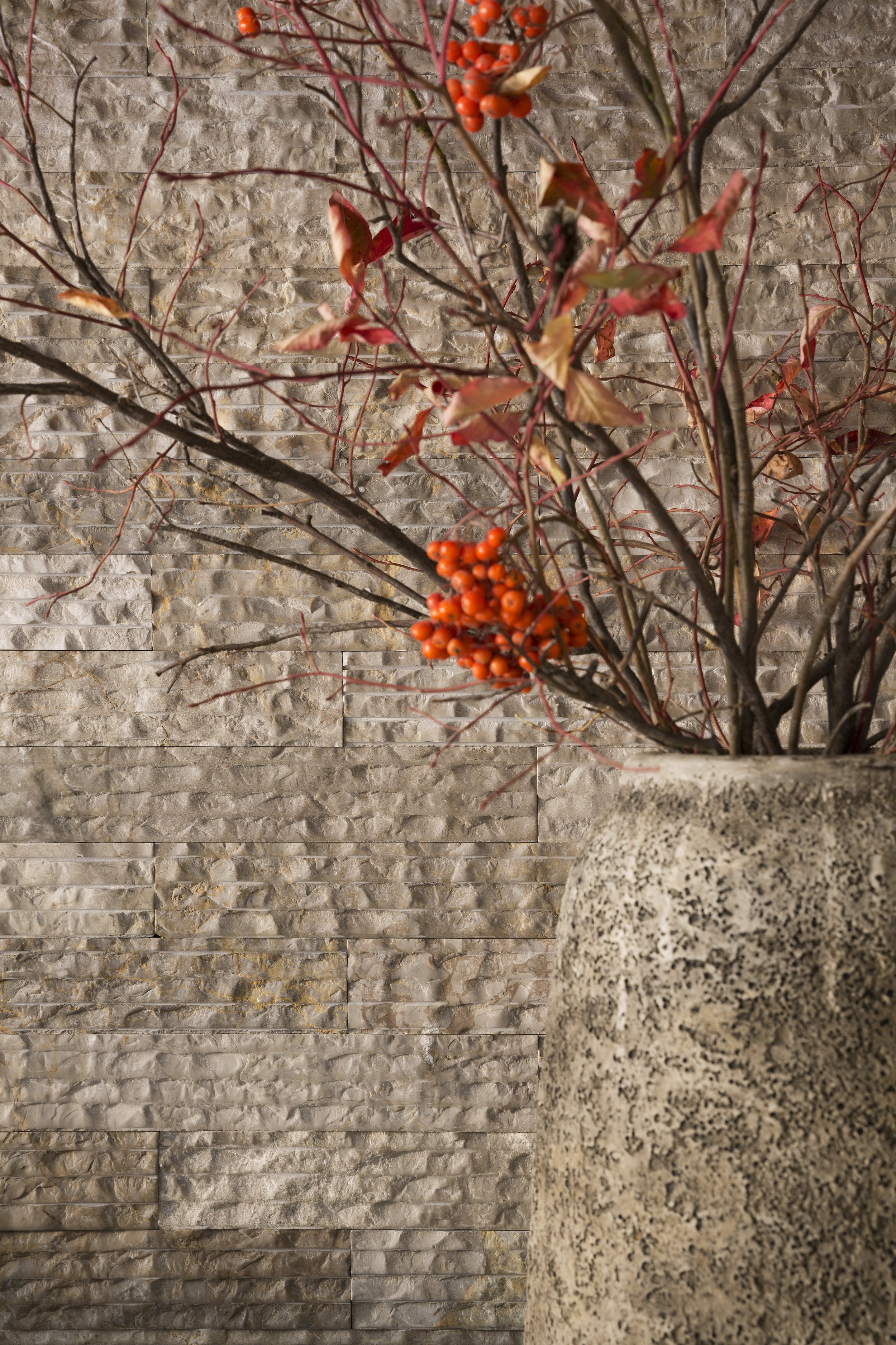 Close-up of a Decorative Vase with a Branch Arrangement featuring red berries against a Textured Stone Wall in an Idaho home